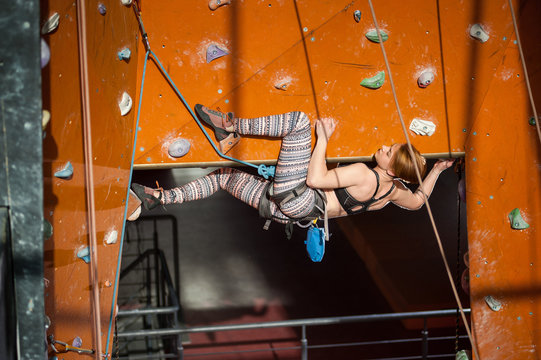 Strong woman with special equipment climbs on an indoor rock-climbing wall