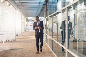 Contemporary African businessman walking on city street with phone