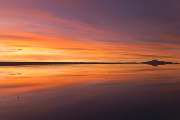 Naklejka premium 雲と山のシルエットが水面に反射するウユニのサンセット。Uyuni gradational sunset, clouds and mountain silhouette reflected surface of the water.