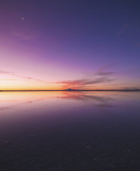 月と紫に染まる空が反射するウユニ塩湖。