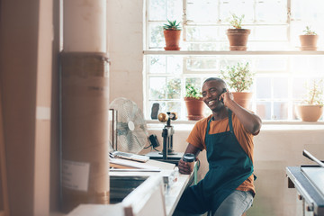 African craftsman, small business owner laughing on phone in studio