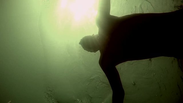 Male Swimmer Creating Water Motion with the Sun Reflecting in the Background. Athlete swimming with the sun reflecting on the waters surface and underwater POV.
