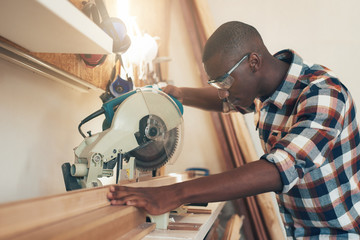 African artisan working with a chop saw in woodwork workshop - obrazy, fototapety, plakaty