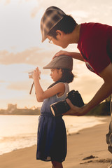 Father teach daughter to take photo on the beach (Warm tone phot