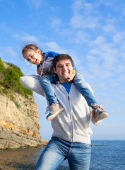 girl sitting on dad's shoulders on sea background