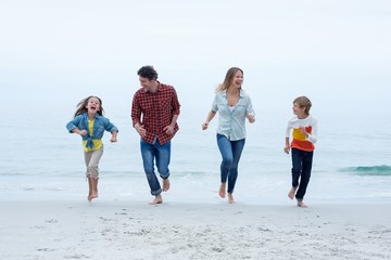 Cheerful family running at sea shore against sky