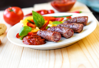 Roasted sausage with bread and vegetables served on white plate and wood board