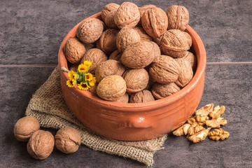 Walnuts in a ceramic bowl and a small bouquet of wild flowers on a dark background