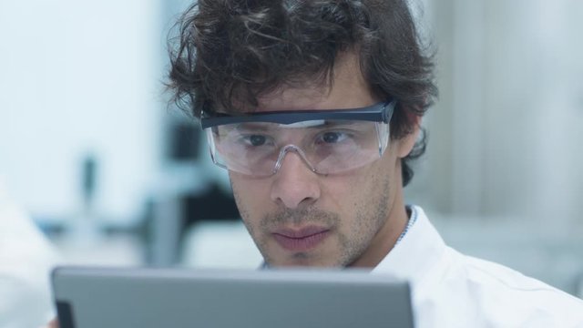 Latin Ethnicity Scientist in Safety Glasses using Tablet Computer in Laboratory. Shot on RED Cinema Camera.