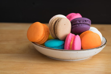 colorful macaroon in white ceramic plate with all flavors on wooden table/colorful macaroon in ceramic plate