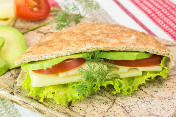 Pita pocket sandwich with cheese, avocado, tomato and lettuce.
