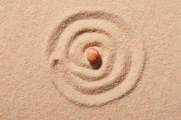 Fototapeta na wymiar Spiral drawn on beach sand with pink round sea stone in centre