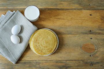 The plate of pancakes, milk and eggs on the napkin, wooden background, copy space, place for text. Carnival.