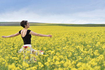 Hipster girl walking through a canola field. Freedom concept