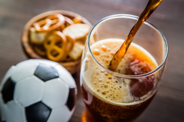 Pouring beer into glass with snacks and football