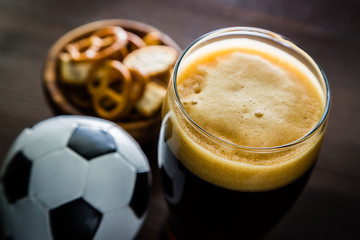 Pouring beer into glass with snacks and football