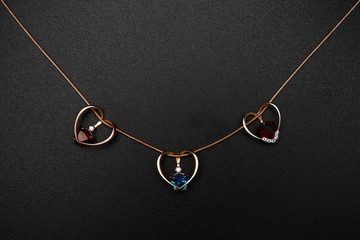 Fototapeta na wymiar Gold heart-shaped pendants with colored topazes on black backgro