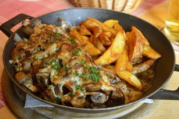 Pork steak with fried mushrooms and onions, gratinated with cheese, served with potato wedges.
