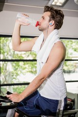 Man drinking water and listening music at spinning class