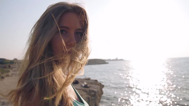 Young attractive blonde woman portrait  near sea and with sun flare behind. Windy hair.