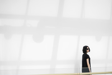 Fototapeta na wymiar Black-haired woman in sunglasses against of sunlit wall with shadow