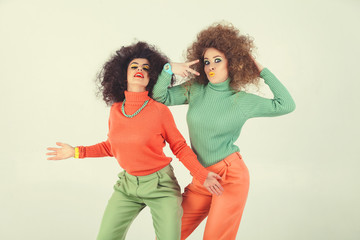 Two funny girls wearing retro clothes in studio. Disco diva over white background