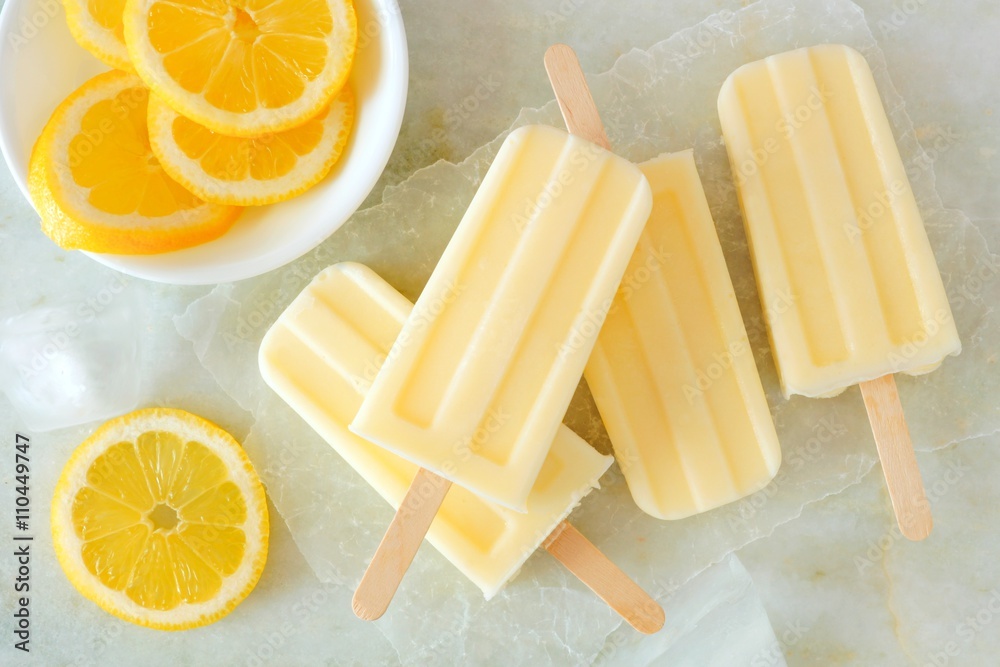Poster lemon vanilla popsicles in a cluster with fresh lemon slices on a white marble background