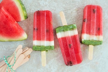 Watermelon popsicles with fresh melon slices on a white marble background