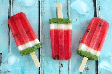 Homemade watermelon popsicles with ice against a rustic blue wood background