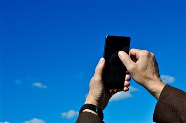 Smartphone in der Hand macht Selfie. Im Hintergrund blauer Himmel