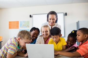 Happy teacher and pupils using laptop