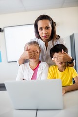 Teacher covering pupils eyes in front of computer 
