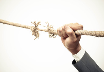 Hand of a businessman hung on almost torn apart rope - Business risk concept