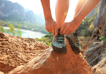 young woman rock climber tying shoelace at mountain rock