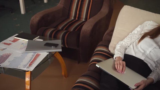 Woman tired and has a break. Caucasian young model. Near female armchair and coffee table with documents and diagrams. 