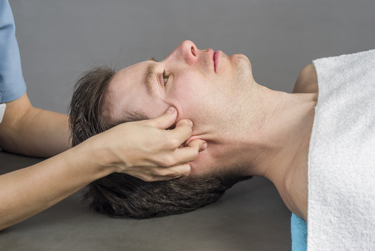 Physiotherapist Doing A Cranial Sacral Therapy To A Man Patient.