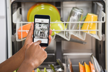 Person Hands Operating Dishwasher With Mobile Phone