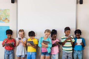 Mixed race pupils standing with technology