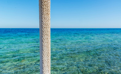wooden pole with rope entwined on a background of blue sea and sky
