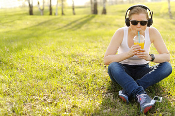 Young woman sitting on grass in Park, listening to music on head