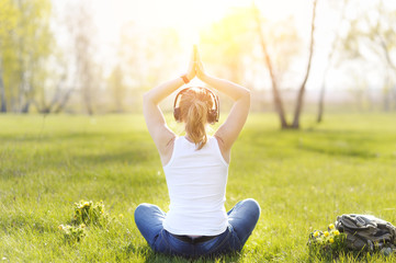Young woman sitting on grass in Park and meditating and listenin