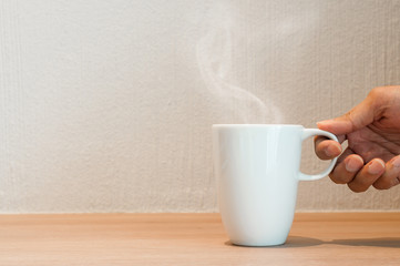 Close up of hand is holding a white cup of coffee.