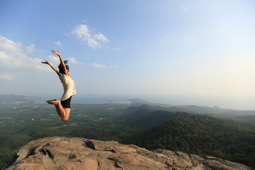 cheering young asian woman jumping on mountain peak rock