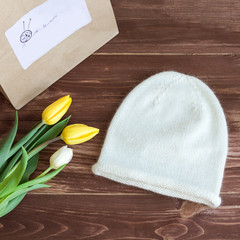 white knitted cap and yellow tulips on a wooden background