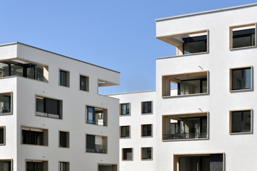 Fragment of white residential buildings with balconies and rectangular windows on a background of blue sky.