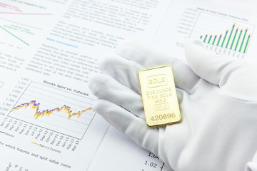 Man right hand with a white handy glove is showing / presenting an one ounce gold bar to a customer...