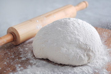 Sprinkle flour into raw bread dough near wooden rolling