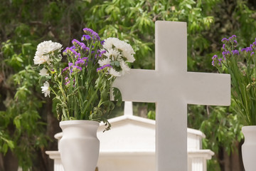 Christian cross on a grave with a flower next to it.
