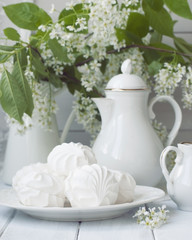 Russian marshmallow or zefir dessert on white plate with branches of blooming bird cherry tree, coffee pot and milk jug on background. Vintage. Toned.