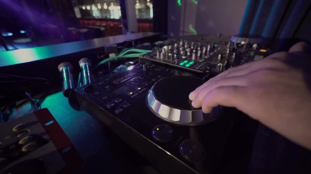 Close-up of DJ hands mixes the track on stage in night club at party